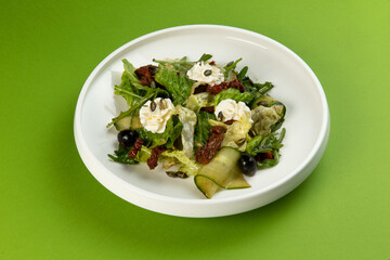 Salad with cucumbers and sun-dried tomatoes in a plate on a green background.