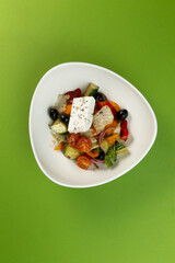 Greek salad in a plate on a green background.