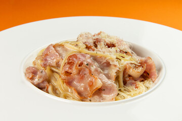 Pasta with bacon in a plate on an orange background.