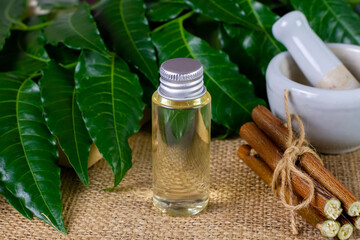 Neem oil in bottle with neem leaf and stick on sackcloth.