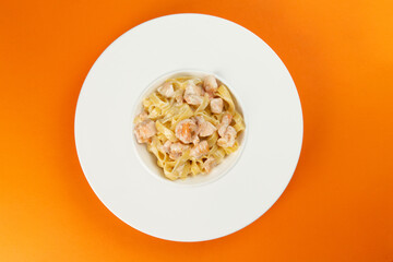 Pasta with salmon in a plate on an orange background.