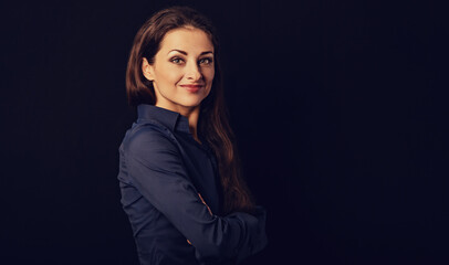 Beautiful thinking serious business woman standing with folded arms in blue shirt on black background with empty copy space for text. Closeup