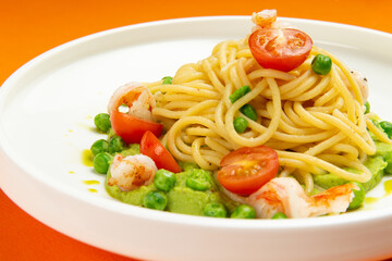 Pasta with shrimp and tomato in a plate on an orange background.