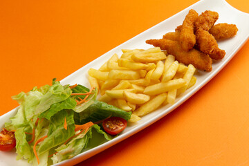 Chicken strips, french fries and salad in a plate on an orange background.