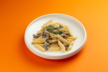 Pasta with mushrooms in a plate on an orange background.