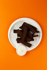 Rye croutons in a plate on an orange background.