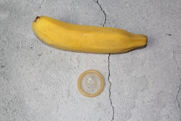 Ripe yellow banana and open condom. Isolated on a gray rustic background, top view. Prevention of...