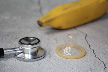 Ripe yellow banana, stethoscope and open condom. Isolated on a gray rustic background. Selective...