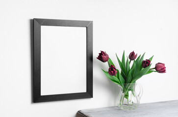 Empty black frame mockup on white wall with fresh red tulips flowers
