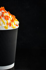 Coffee with candied fruit and cream in a paper cup. on a black background. Free space for text.