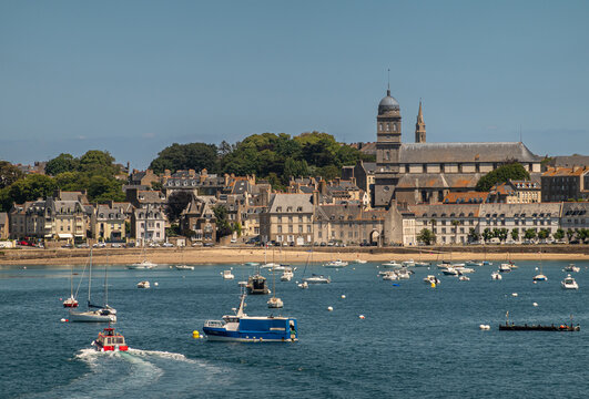 St. Malo, Brittany, France - July 8, 2022: Cityscape of Saint-Servan neighborhood at its beach on Rance river mouth Sainte-Croix church under blue sky. Yachts and small ferries up front