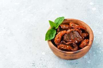 Sun-dried tomatoes in a wooden bowl. On a concrete background.