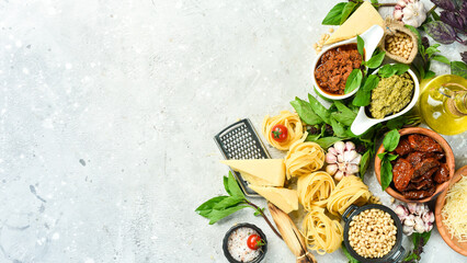 Preparation of spaghetti: pesto sauce, pasta, basil, parmesan and nuts, olive oil. On a concrete background. Top view.