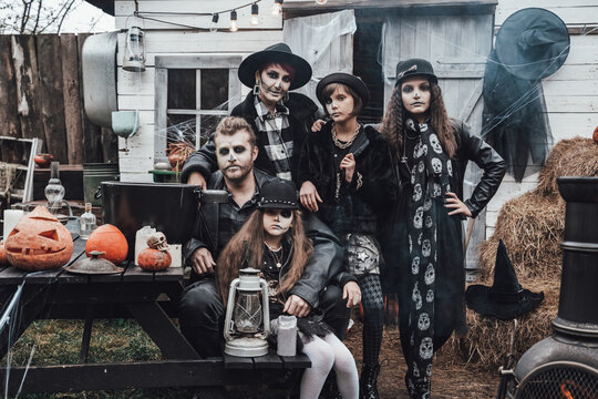 Scary family, mother, father, daughters celebrating halloween. Terrifying black skull half-face makeup and witch costumes, stylish images.Horror,fun at children's party in barn on street.Hats,jackets
