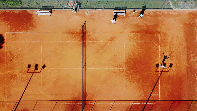 Tennis court drone aerial shot vertical top view, overhead shot of a player shadow silhouette  tennis player on a juicy red coating