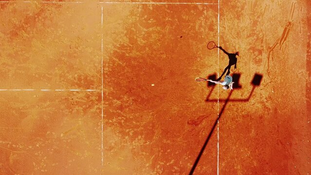 Tennis court drone aerial shot vertical top view, overhead shot of a player shadow silhouette  tennis player on a juicy red coating