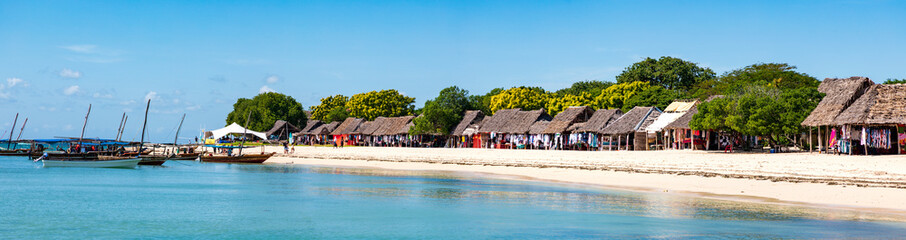 Sansibar, Kwale Island  an der Küste der Insel. Dhows, Holzhütten  am Strand, blauer Himmel und türkis-blaues Wasser,  Panorama.