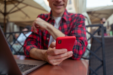 Mid aged man in plaid shirt sitting at the table in the street cafe with a phone in hands