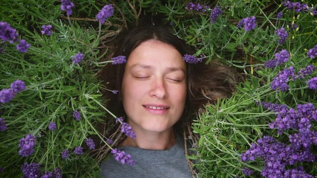 Connecting with nature. Young happy woman lying among lavander flowers in blossom field. Female without makeup relax on the grass on sunny summer day.