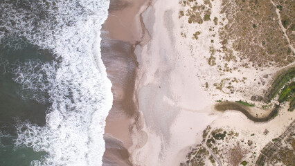 Fototapeta na wymiar Aerial view of the sea, beach boulders, pebble shore, and waves. Sea waves breaking on rocks. Sunny beach with sand dunes and blue sky in Esposende, Portugal. Spring Day.