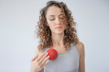 Curly woman performs a myofascial release on the chest muscles using a red ball with spikes....