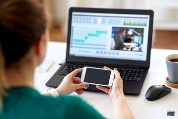 technology, post production and vlog concept - close up of woman with smartphone and laptop computer working at home office