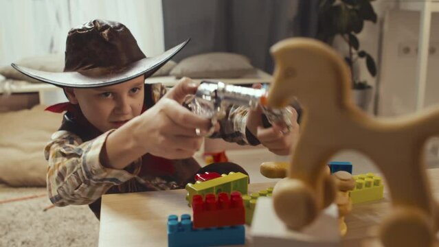Medium of Caucasian boy dressed as cowboy shooting toy guns in playroom