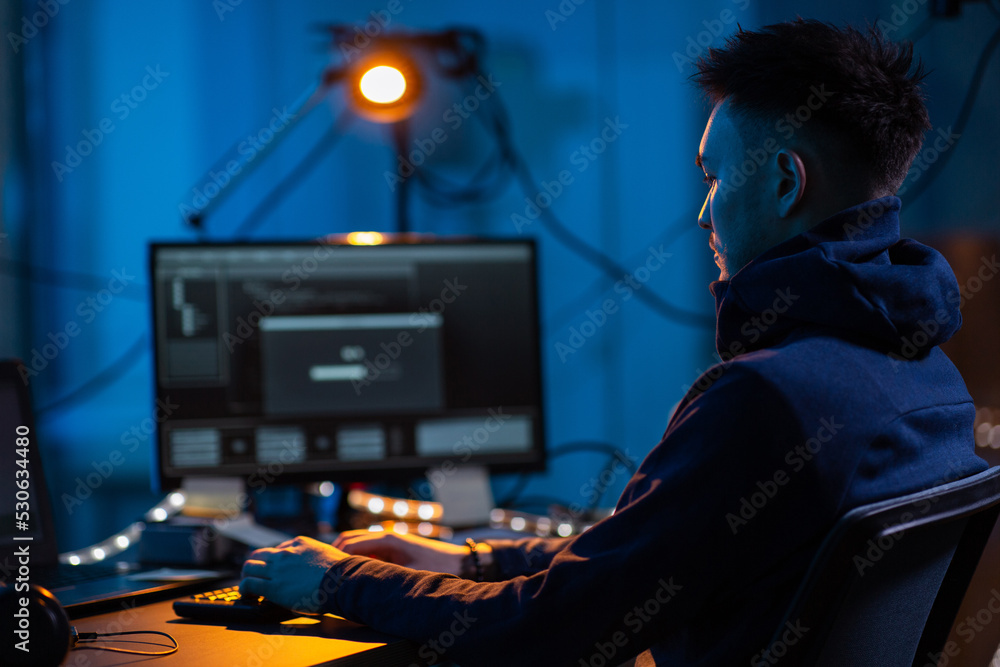 Poster cybercrime, hacking and technology concept - male hacker in dark room writing code or using computer