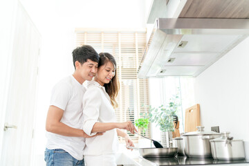 happy asian couple cooking healthy food. beautiful attractive girlfriend hugging by cheerful husband preparing healthy meal. couple cooking together for delightful beautiful healthy fresh good recipe