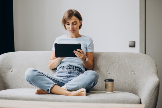 Woman sitting home on a sofa and reading book on a tablet