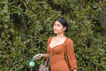 A beautiful young woman holds her phone and her handbag while walking to her office early in the morning.