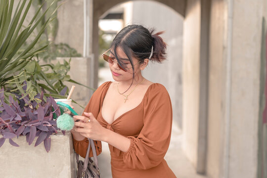 A young Filipino woman surfs the net on her cellphone while waiting for her driver to fetch her.