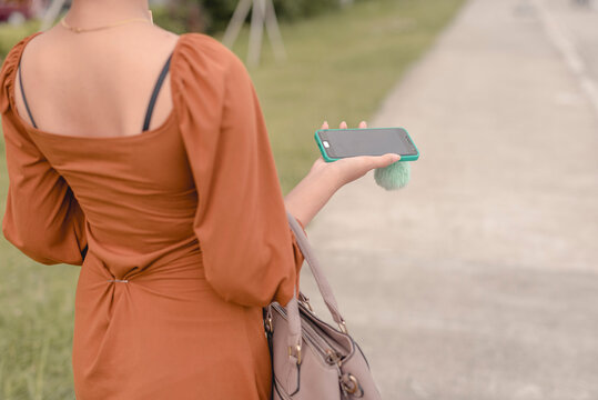 Woman holding a phone on her right hand while carrying a hand bag. Walking on the street while talking to a friend on the phone on speaker.