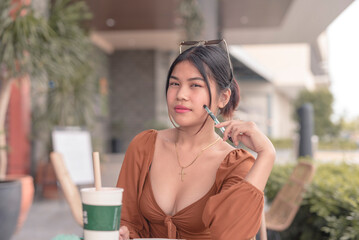 A gorgeous lady sitting outside the coffee shop poses for the camera while holding the pen against...