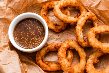 Breaded onion rings with sauce. Served in a wicker basket on craft paper.