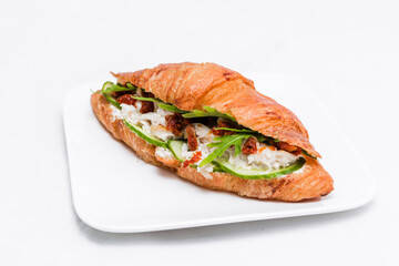 Croissant with squid meat, cheese, fresh cucumber, sun-dried tomato and lettuce arugula on a white background.