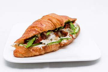 Croissant with squid meat, cheese, fresh cucumber, sun-dried tomato and lettuce arugula on a white background.