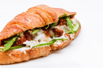 Croissant with squid meat, cheese, fresh cucumber, sun-dried tomato and lettuce arugula on a white background.