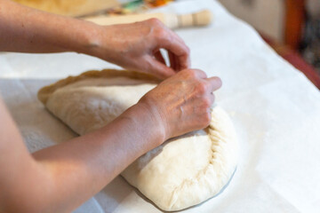 Women's hands sculpt from the dough a large pirok with potatoes and msyaom. Home national cuisine
