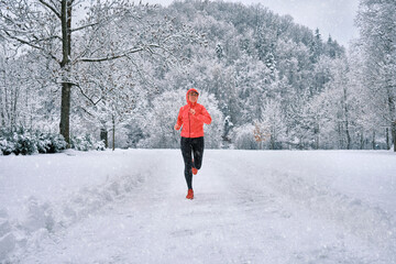 Running woman, girl runner on snow in park in winter sunny day. Female in pink sportswear jacket...