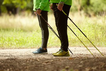 Cropped image of woman and man walking with Scandinavian sticks in autumn forest, outdoors. Nordic...