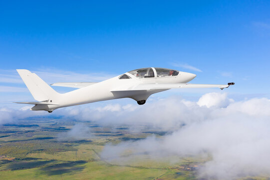 The glider is flying over the clouds and fields of the rural landscape.