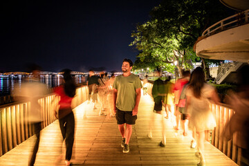 Turista paseando de noche por puente peatonal iluminado rodeado de gente desenfocada por el...
