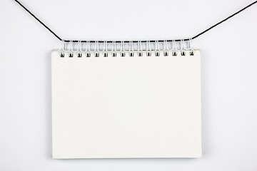 White blank notepad blank hanging on a rope on an isolated white background. White notepad mockup, copy space notebook.