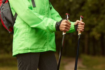 Cropped image of woman in light sports jacket holding Scandinavian sticks, getting ready to Nordic walking. Healthy lifestyle, professional sports equipment