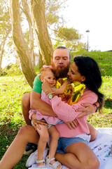Fototapeta premium white man with red beard, Venezuelan woman and red-haired girl having picnic in city park at sunset
