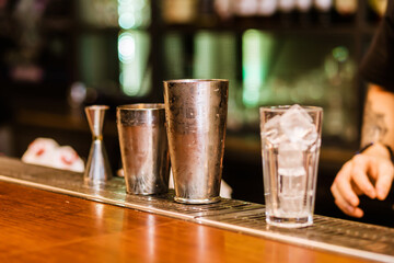 There is a shaker and a glass of ice on the bar counter. The glass is cooled to serve a cocktail