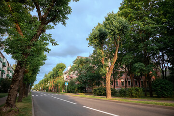 Street view landscape old city, little houses on sunset. Old pink cottage in cozy quiet town. Old architecture street view. Calm old town street with green trees. City road and crosswalk without cars.