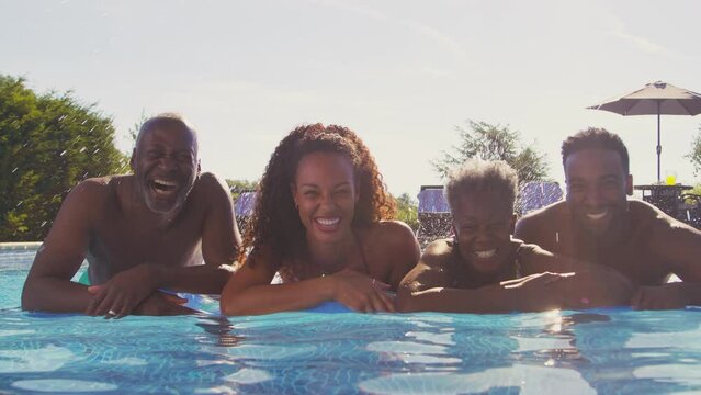 Portrait of smiling multi-generation family with adult offspring on summer holiday relaxing in swimming pool floating in inflatable airbed - shot in slow motion