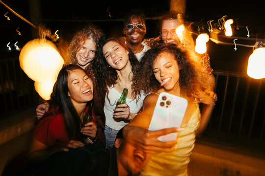 Friends are taking selfies at the rooftop nighttime party.